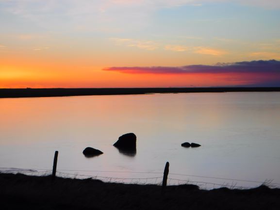 Morning light turns a tranquil lake pale orange on Iceland's south-west coast 