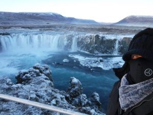 A photo of me covered from head to toe in winter weather gear whilst standing in front of an icy Godafoss